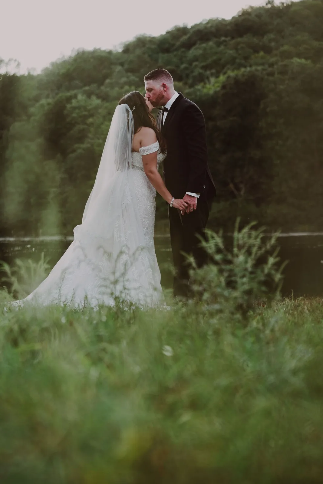 Bride and groom sharing a kiss in a grassy field by the water at dusk — Maximus Visions wedding photography, New Jersey & New York City
