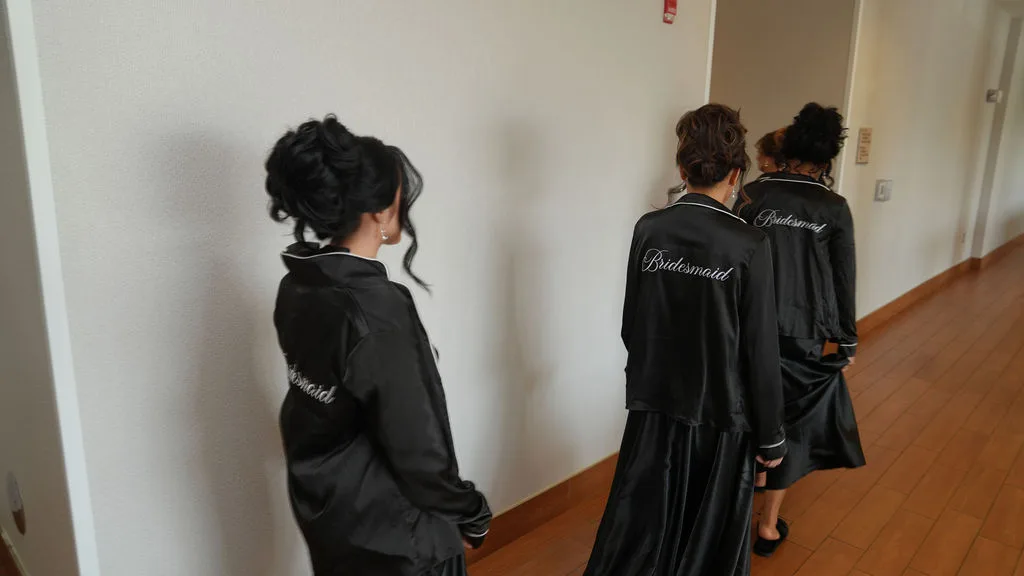 Bridesmaids in monogrammed black robes head down the hallway — a quiet beat between getting ready and go time, New Jersey
