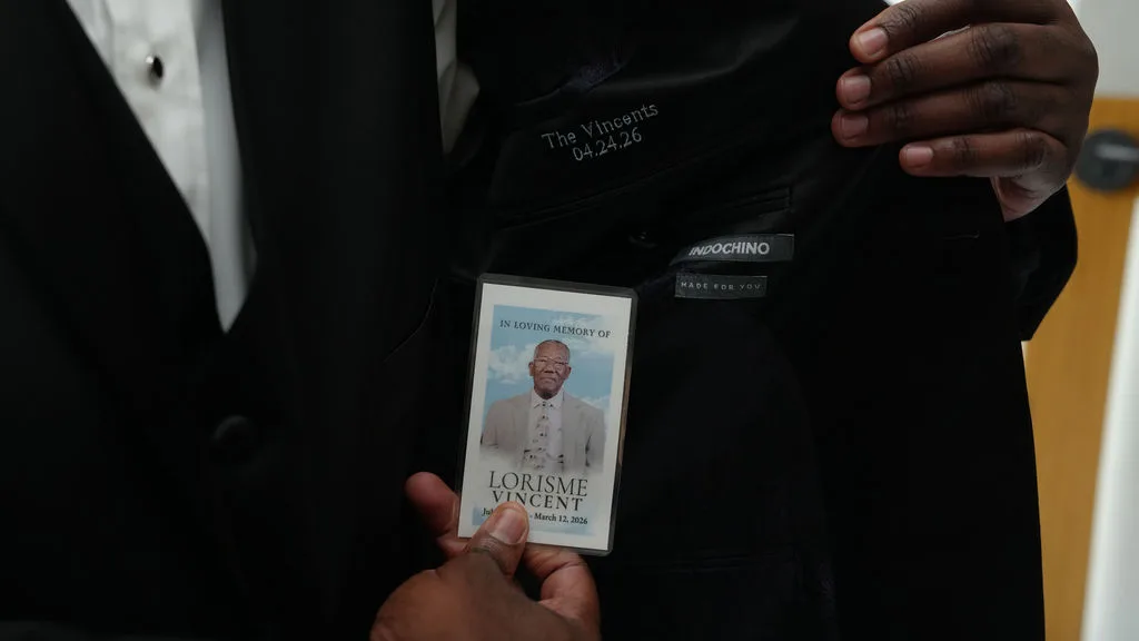 Tre holds a memorial card over his heart while dressing — a quiet tribute on the wedding day, New Jersey