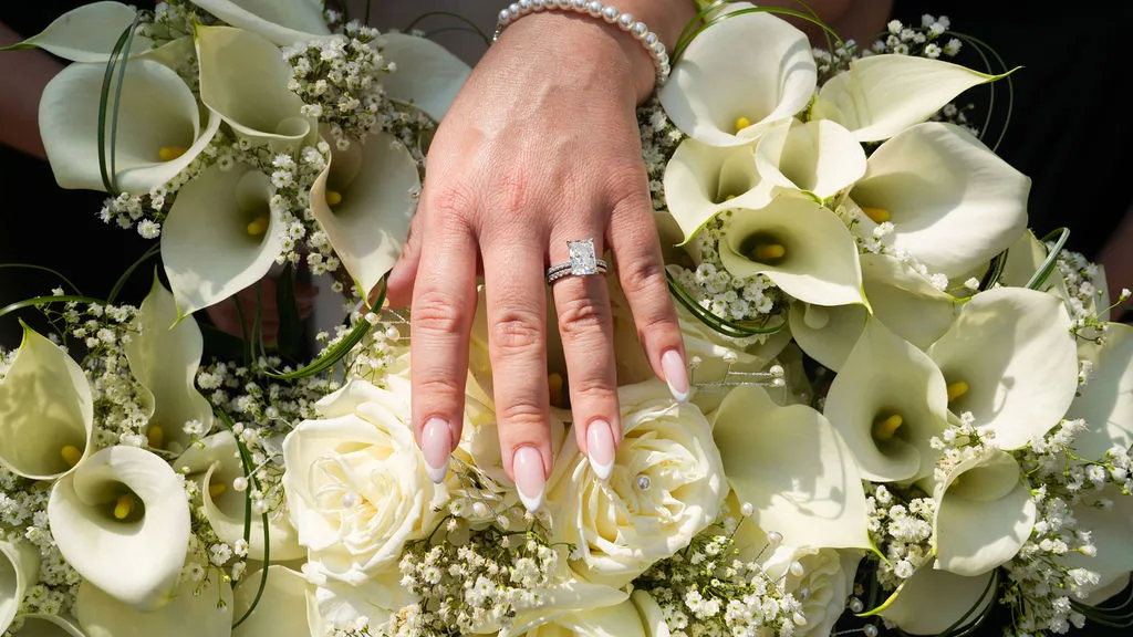 Becky's wedding rings and pearl bracelet over a bouquet of calla lilies, white roses, and baby's breath — fine-art detail, New Jersey wedding