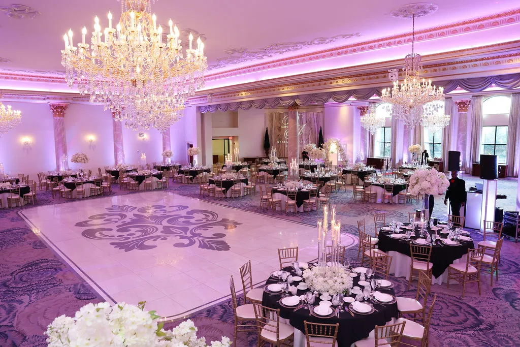The reception ballroom under crystal chandeliers — black linens, white florals, and a monogrammed dance floor, New Jersey wedding