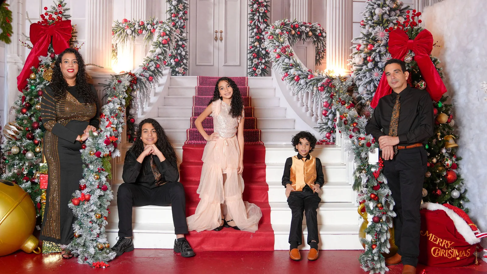 Family of five in holiday formal wear on a grand staircase set with garlands and red bows — Maximus Visions holiday portrait session, New Jersey & New York City
