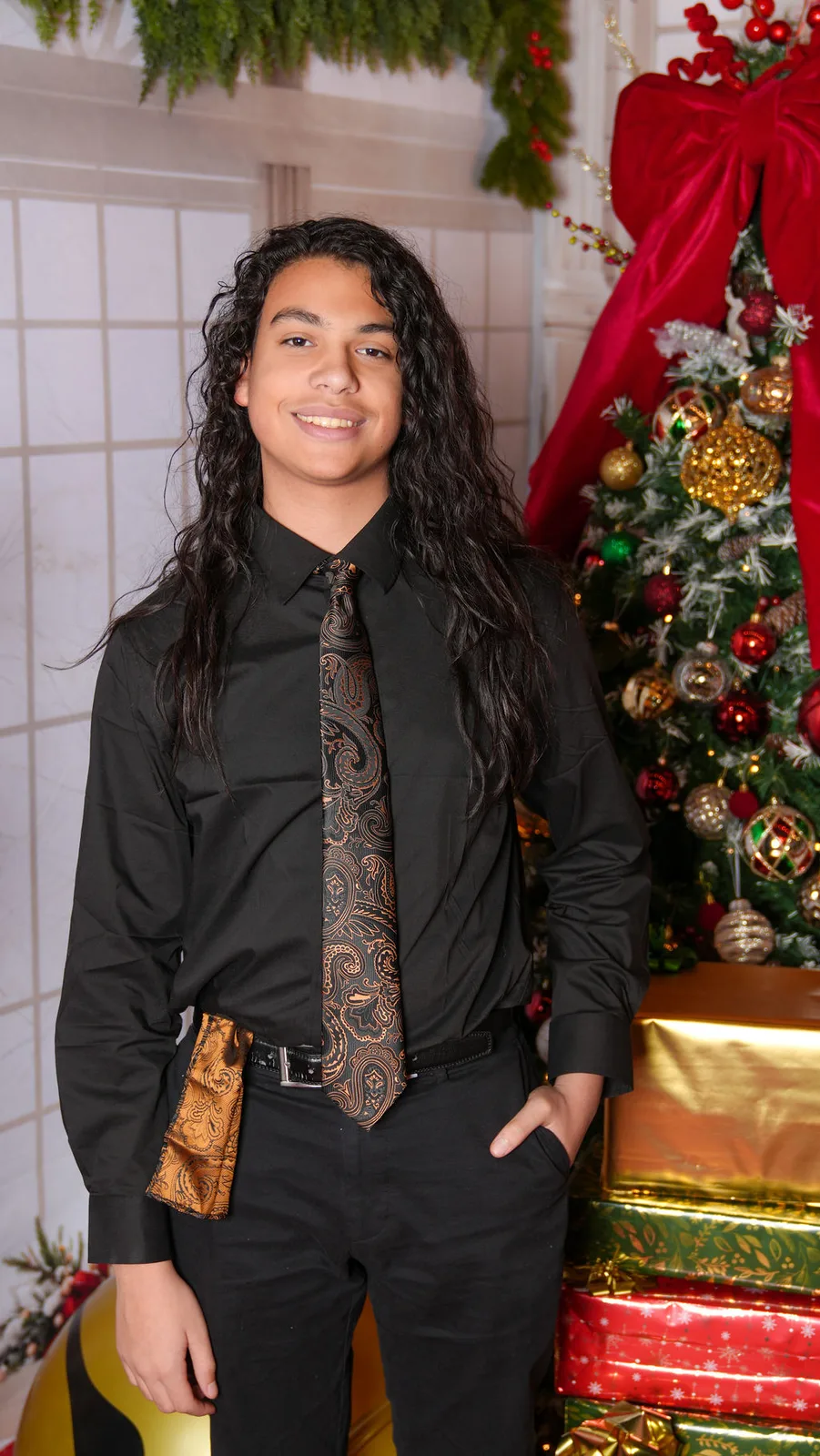 The eldest Marlin son, long-haired and sharp in black with a gold tie, on the garlanded staircase set — holiday portrait by Maximus Visions, New Jersey