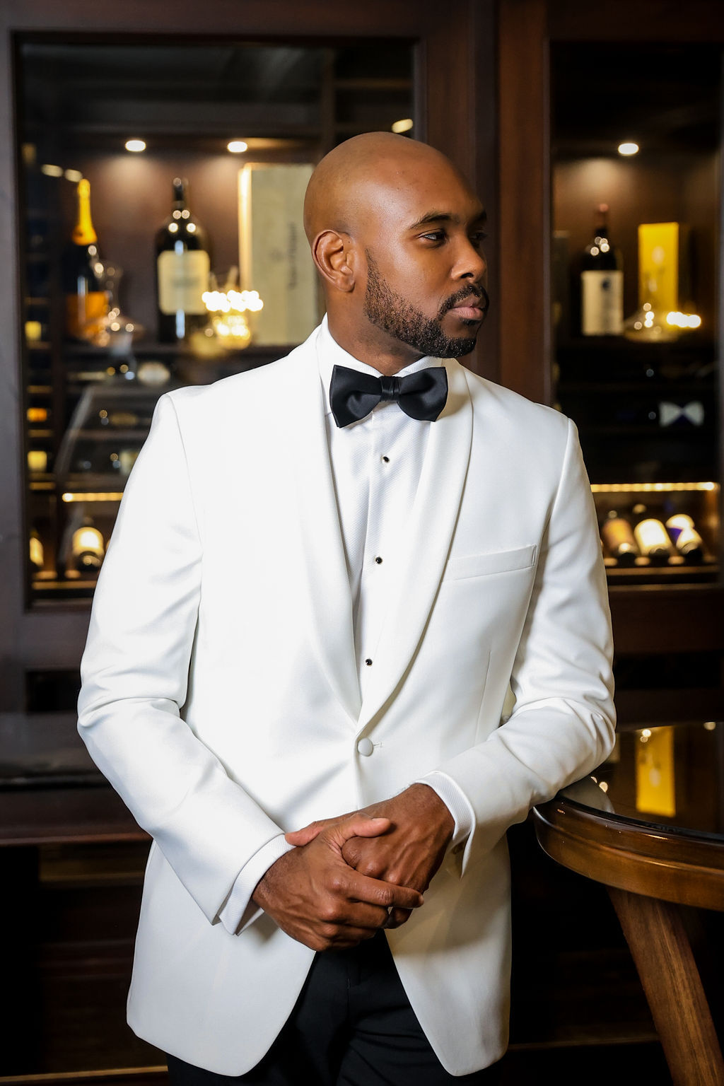 Groom in white shawl-collar tuxedo with black bow tie in the estate wine cellar, NJ wedding portrait