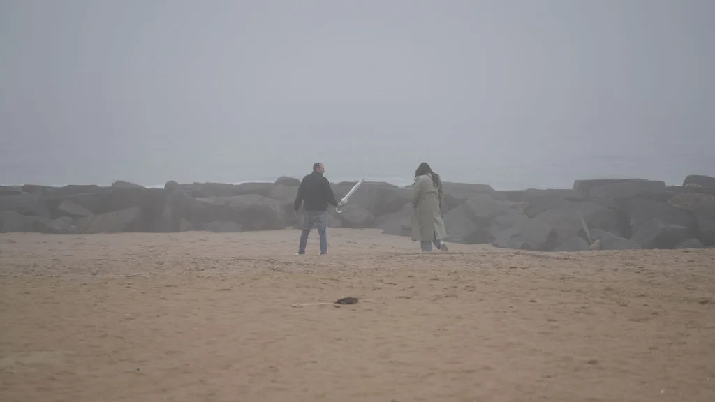 A couple walks the empty fog-covered beach toward the stone jetty — surprise proposal photography by Maximus Visions, New Jersey