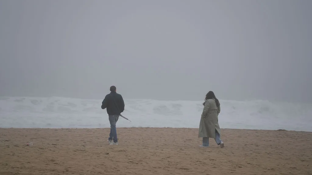Two figures cross the wide grey sand under heavy sea fog on the New Jersey shore