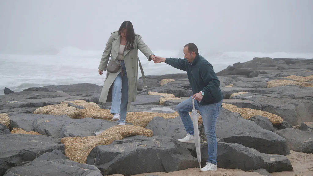 Hand in hand across the stones, umbrella tucked under his arm — documentary proposal photography, New Jersey