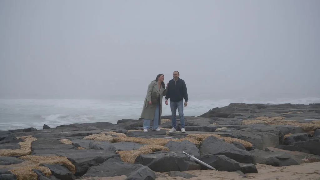 Laughter on the rocks with the surf crashing below — candid proposal-day moment, New Jersey shore