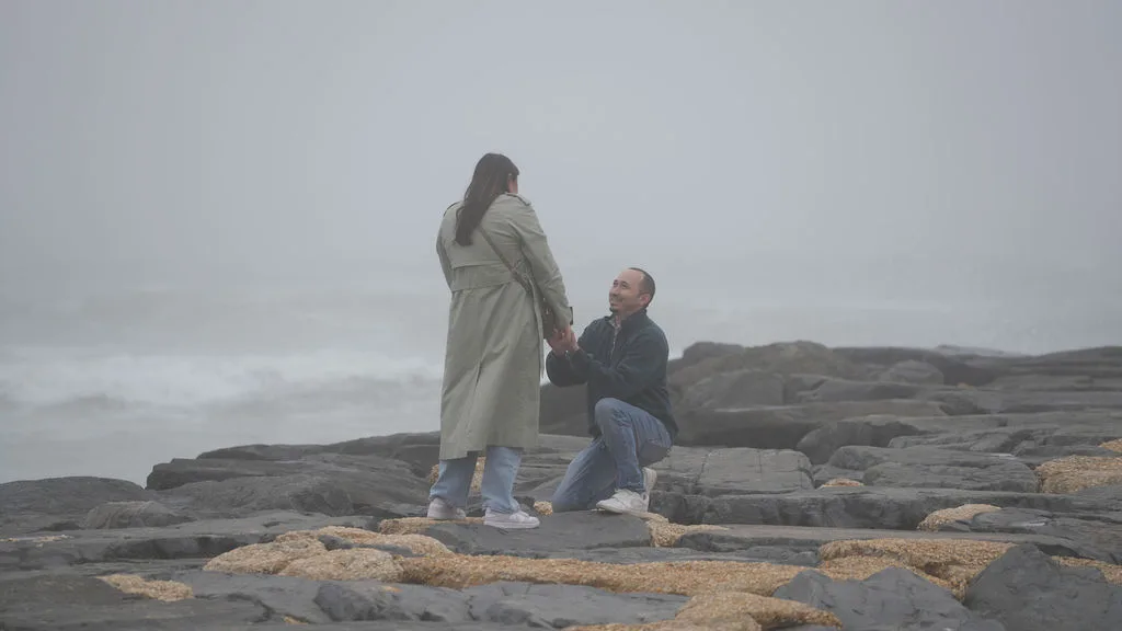 Down on one knee, he holds her hand and looks up at her, smiling — surprise proposal photographed by Maximus Visions, New Jersey