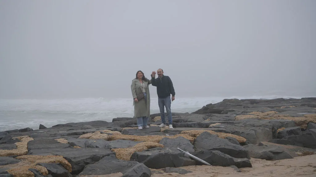 Hands raised in triumph on the jetty, the fog and ocean behind them — she said yes, New Jersey